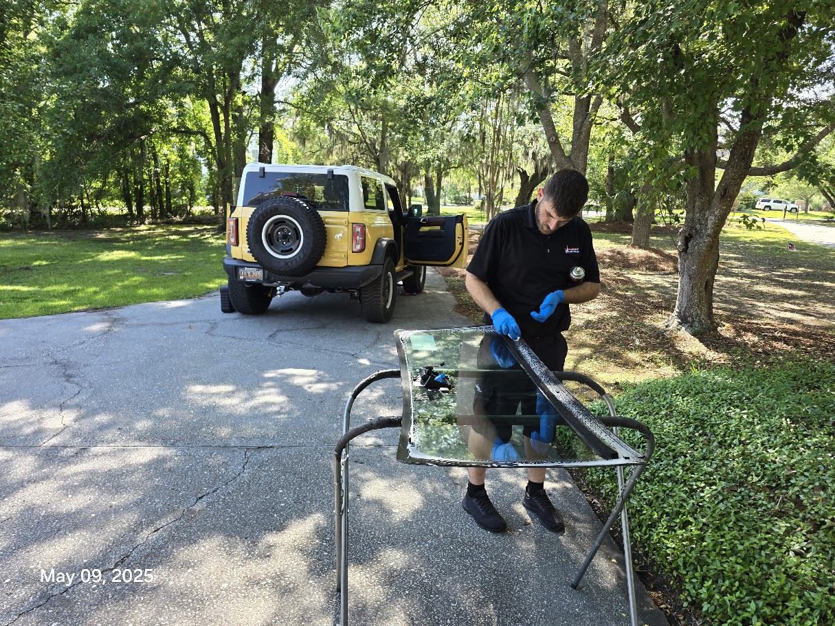 Mission Auto Glass technician preparing replacement windshield glass with Ford Bronco in background